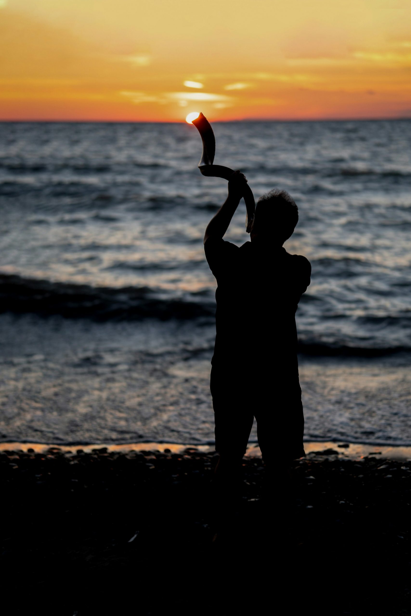 A man blows a shofar at sunset on a beach